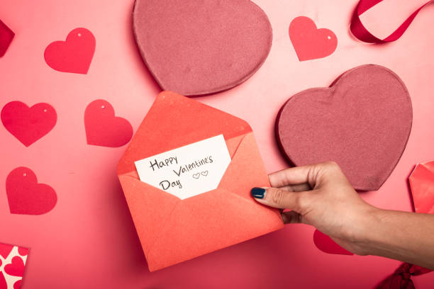 istock A flat lay Valentine's Day composition on a pink background featuring red and pink heart-shaped gift boxes, envelopes, paper hearts, a ribbon bow, and a handwritten love note in an open envelope 2200570843