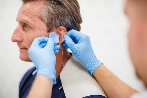 istock Mature Male Audiologist Fitting Hearing Aid 2200573173