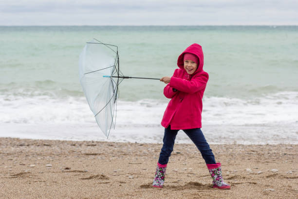 Caucasian child of 7 8 years holding broken umbrella because of wind on sea shore