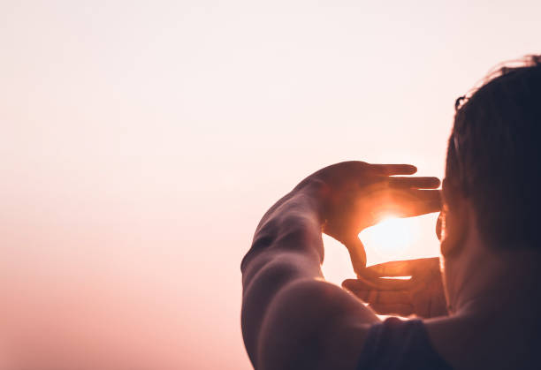 istock Man framing the sun with hands at sunset 2200583945