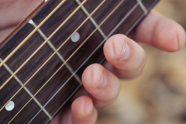 A close-up shot of a guitarist's hand pressing down on the frets of an acoustic guitar. The blurred, colorful background lights add a dynamic and artistic feel, evoking the essence of live music, creativity, and passion for playing the guitar