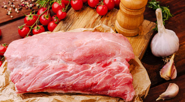 istock Fresh pork cut on wooden board with garlic and cherry tomatoes in rustic kitchen setting 2200589287