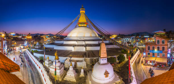 The iconic mandala dome of Boudhanath stupa, spotlit beneath dusk skies as crowds of pilgrims and tourists walk around the ancient Buddhist shrine, a UNESCO World Heritage Site in Kathmandu, Nepal's vibrant capital city.