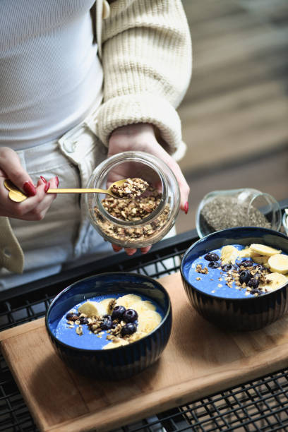istock Female Arranging Blue Smoothie Bowls Adding Homemade Granola on Top 2200596123