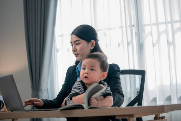 istock Busy mother working on laptop while caring for infant in a well-lit home office environment during daytime 2200598532