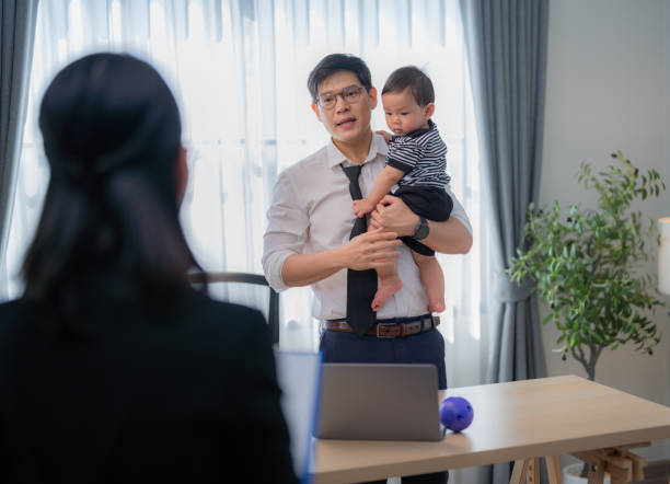 istock Father holds baby while discussing work in a modern home office during daylight hours 2200601448