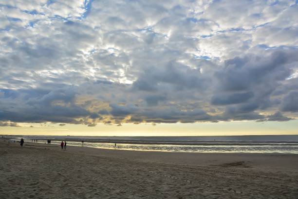 istock People on the beach walk under cloudy sky where water meets shore 2200608119