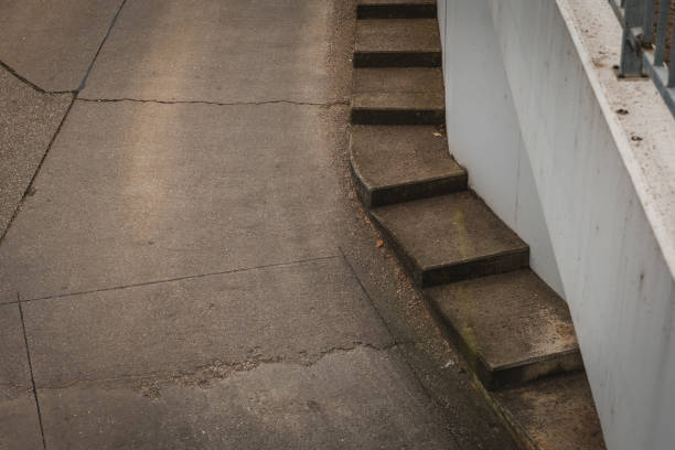 A series of concrete steps winds down a curved path in an urban environment. The late afternoon sun casts soft shadows, highlighting the textures of the surfaces.