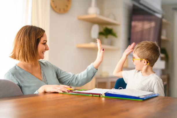 istock homework and school concept - smiling student boy with book writing to notebook at home with his mother help her 2200614505