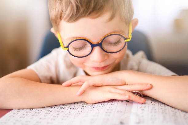 A homework and school concept - smiling student boy with book writing to notebook at home