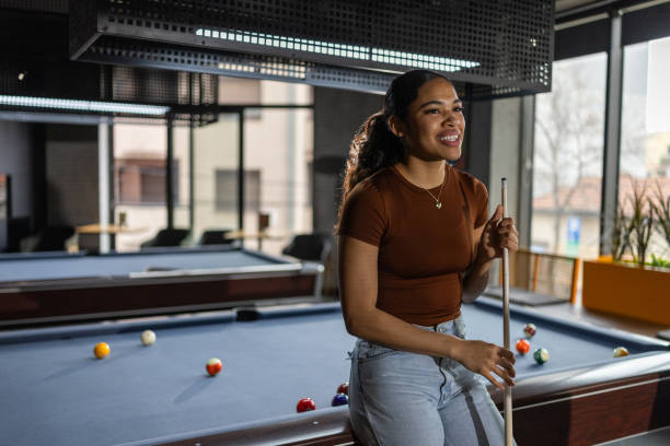 Portrait of beautiful young woman leaning on pool table while relaxing in a local pool hall