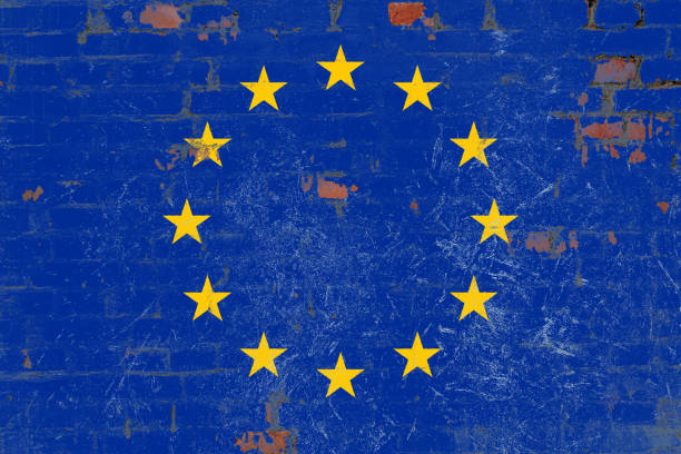 A depiction of the European Union flag painted on a brick wall with a distressed and weathered texture. The vibrant blue background with yellow stars contrasts with the rough surface, symbolizing unity and endurance.