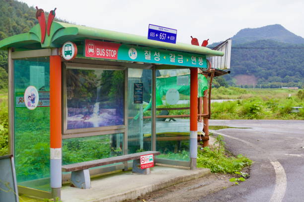 Goesan County, South Korea - September 9, 2020: A small rural bus stop with colorful signage and a scenic waterfall image provides shelter for travelers along a quiet countryside road near Yeonpung.