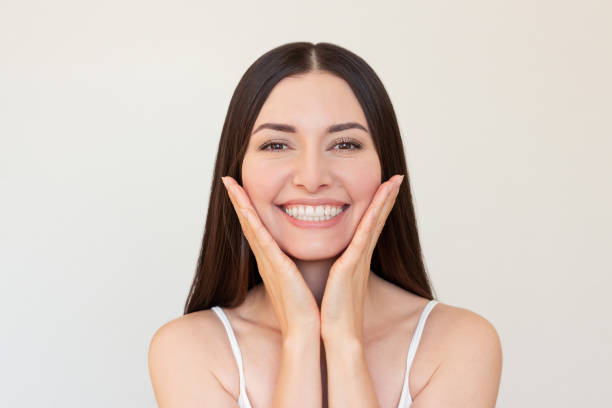 istock Young brunette woman looking at camera, smiling and gently touching her face with both hands 2200618562