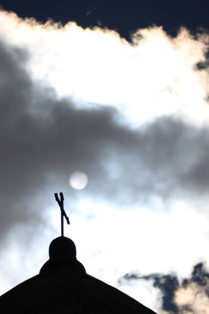 Silhouette of a church cross against a dramatic cloudy sky, capturing a serene and spiritual moment.