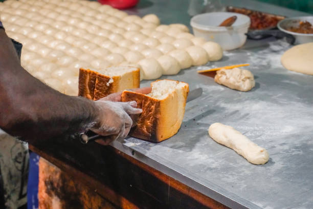 Stock photo of baker expertly cuts through freshly baked, golden-colored bread rolls with a sharp knife. The soft dough inside contrasts beautifully with the crispy, golden crust. The baker’s hand shows the skillful precision needed to create these perfect bread rolls