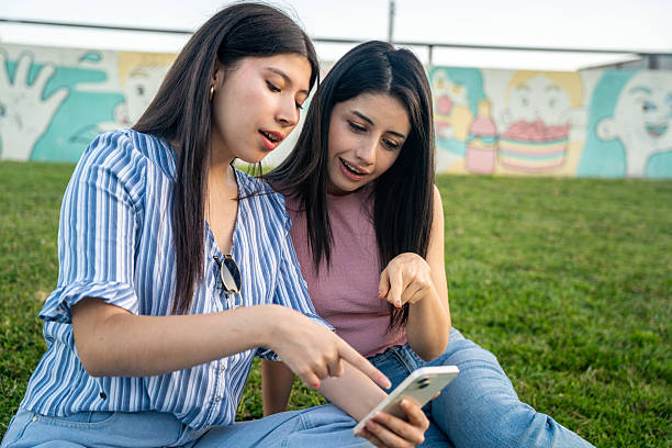 istock Two young women sit on the grass, looking at a cell phone 2200632855