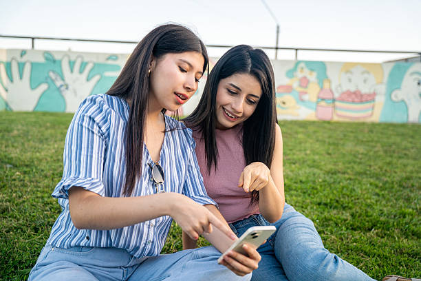 istock Two young women sit on the grass, looking at a cell phone 2200632891