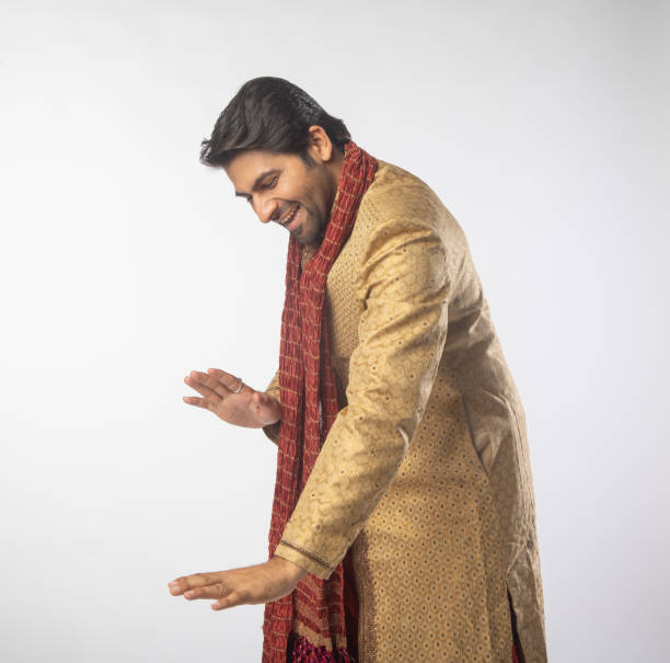 Excited young groom dressed in traditional clothing dancing against white background during wedding ceremony