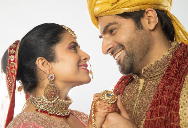 Close-up of romantic bride and groom in traditional clothing holding hands and looking at each other against white background