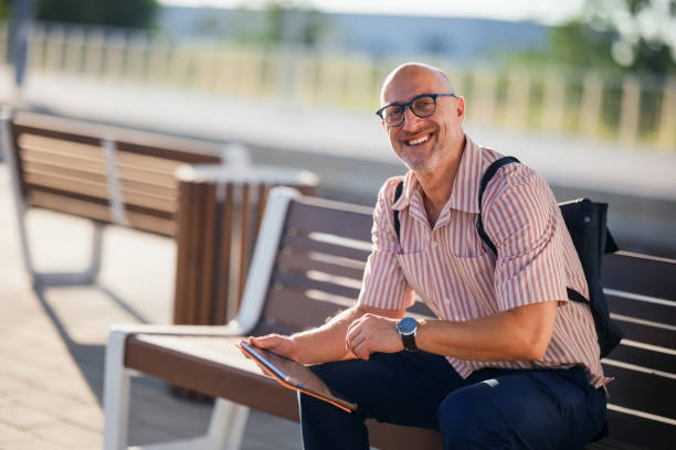 istock Smiling Man Relaxing Outdoors Holding Tablet on a Park Bench 2200646640