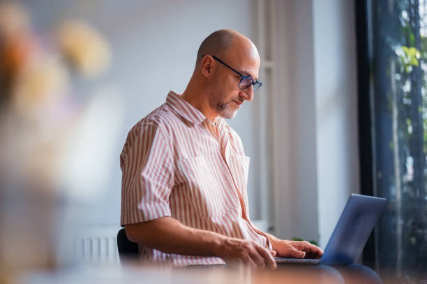 istock Senior Professional Working on Laptop in Sunlit Office Space 2200646647