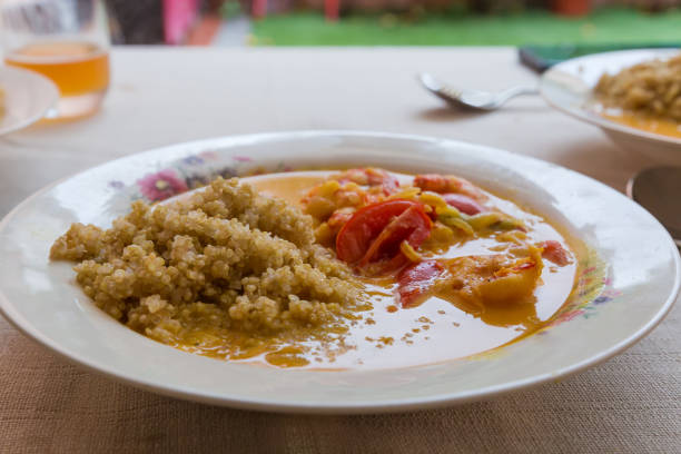 Portion of porridge of white quinoa seeds with souse of shrimps and tomatoes on the dish on table covered with white tablecloth, front view in selective focus
