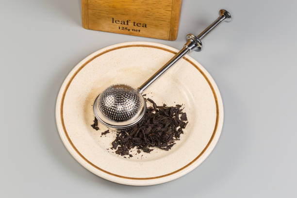 istock Stainless steel tea strainer on saucer with black tea leaves 2200654513