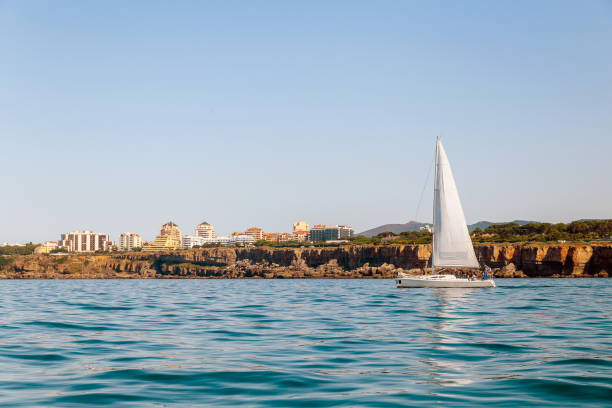 istock Sailboat Near Coastal Town with Cliffs and Clear Blue Sky 2200654736