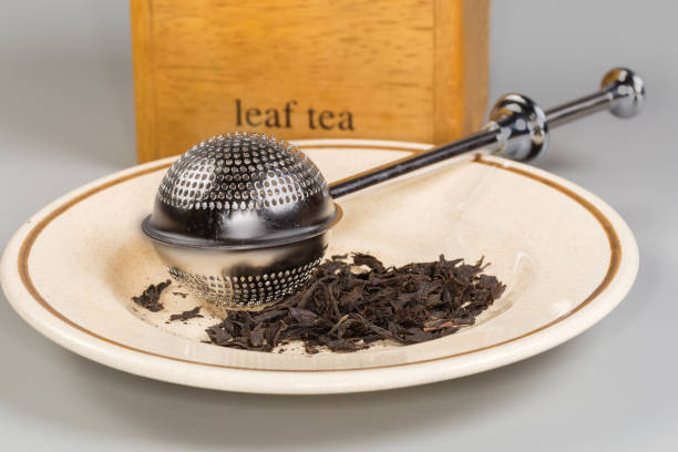 Stainless steel tea strainer on saucer with black tea leaves