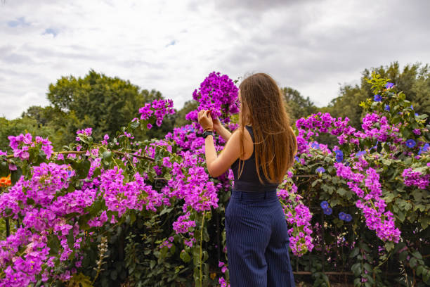 With her back to the camera, a woman reaching out to a cluster of purple flowers