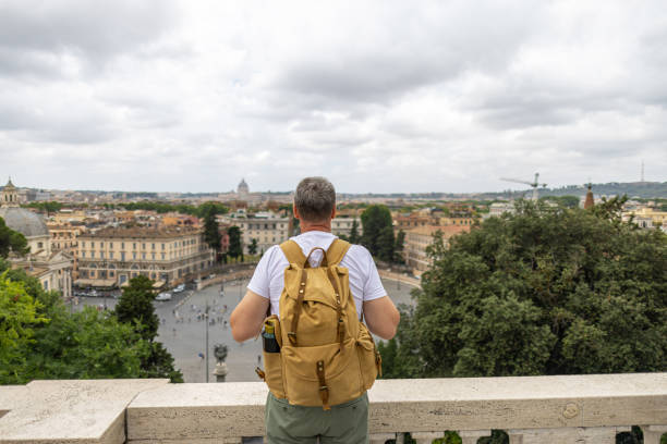 istock Rear view of man with backpack standing and looking at view in Rome 2200656395