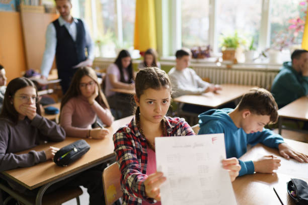 Schoolgirl showing her F grade on a test at school Unhappy schoolgirl showing her F grade on a test at school and looking at camera report card letter f test results education stock pictures, royalty-free photos & images