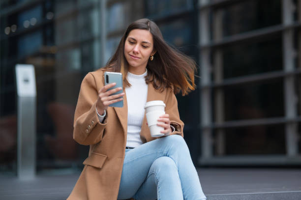 istock Businesswoman using smartphone and drinking coffee outdoors 2200659882