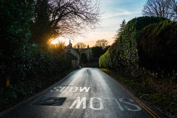 Road leading into castle combe at sunset with slow marking painted on the tarmac