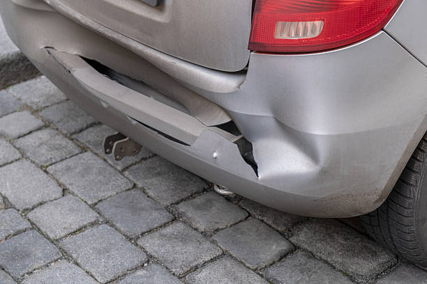 istock Damaged silver car bumper is broken with visible cracks and dents, indicating an accident. The vehicle is parked on a cobblestone street, showing clear signs of a previous collision. 2200670968
