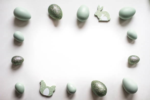 Frame of pastel green Easter eggs, glitter eggs and animal figures in the shape of a hen and a bunny on white background. Flat lay, top view, copy space