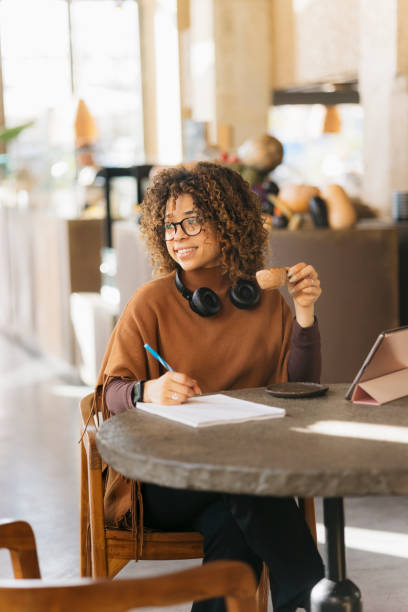 istock Young woman working remotely in a coffee shop is writing on a notepad while drinking a coffee 2200691573