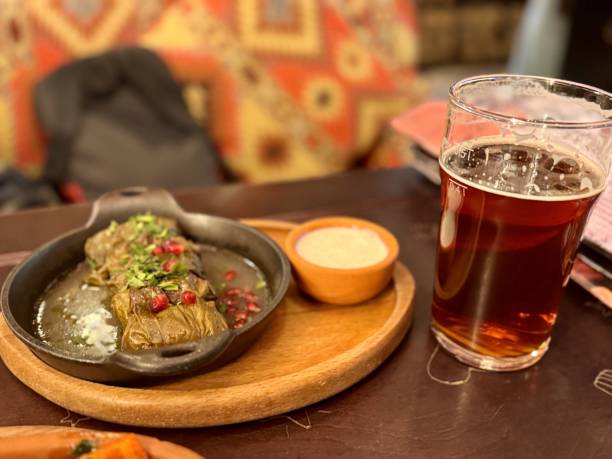 istock Delicious dolma (sarma) stuffed with grape leaf rice, with white yogurt sauce and pomegranate seeds. Lebanese dolma sarma has a glass of light beer on a wooden plate next to it. Close-up 2200696196