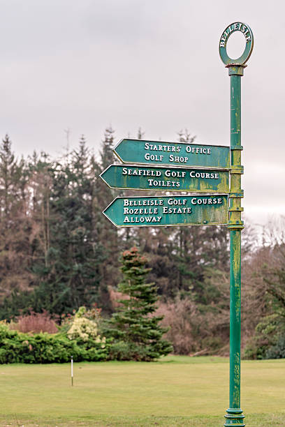 A weathered, green-painted metal signpost in Belleisle Park, Ayr, UK on February 15, 2025 that directs visitors to the golf shop, starters' office, Seafield Golf Course, toilets, Belleisle Golf Course, Rozelle Estate, and Alloway.