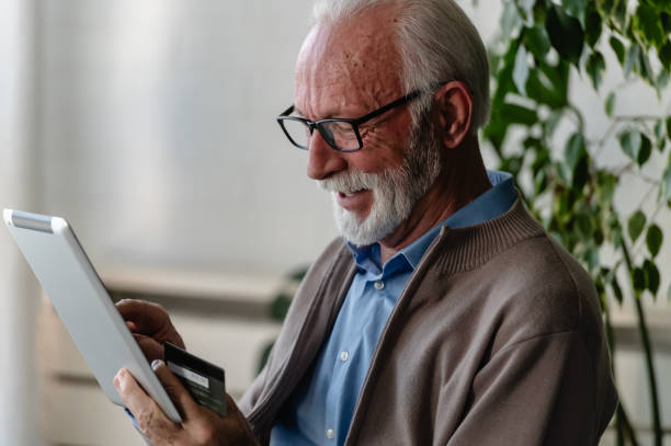 istock A happy elderly man with glasses and a beard uses a tablet while holding a credit card, smiling as he shops or makes an online payment at home 2200699808