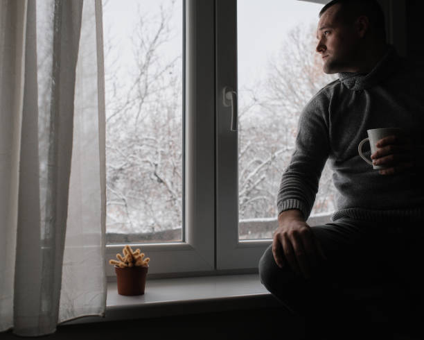 istock A young handsome man sits by the window and drinks his morning coffee. It's a winter idyll outside. 2200699990