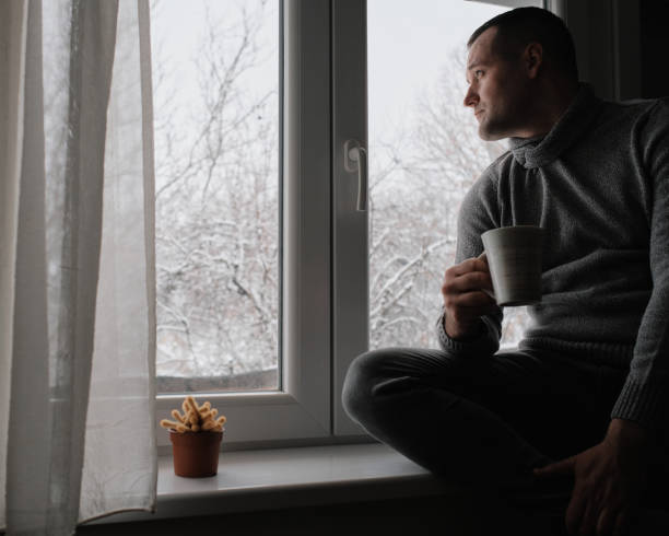 istock A young handsome man sits by the window and drinks his morning coffee. It's a winter idyll outside. 2200700053