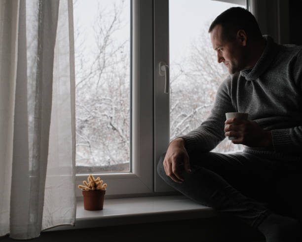istock A young handsome man sits by the window and drinks his morning coffee. It's a winter idyll outside. 2200700110