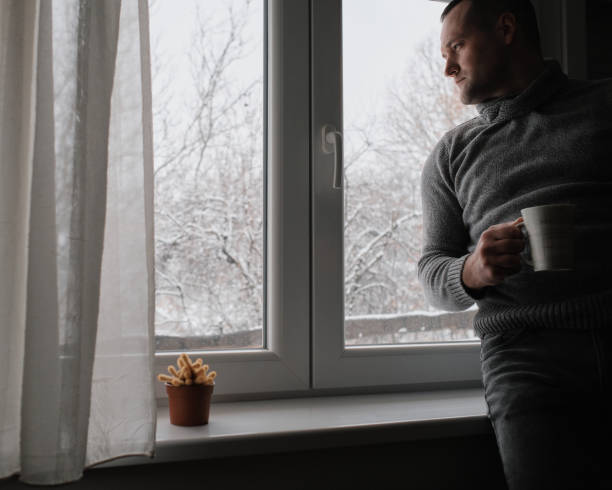 istock A young handsome man sits by the window and drinks his morning coffee. It's a winter idyll outside. 2200700269
