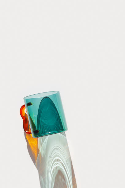 istock Colorful Glass Mug with bright sunlight Shadows, transparent teal colored mug casting dynamic, vibrant light reflections and shadows on light white surface, creative aesthetic top view, minimal photo 2200719682