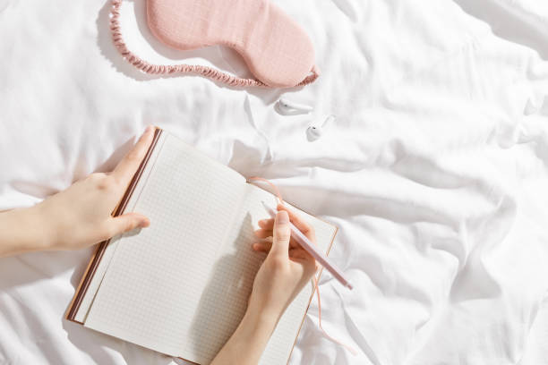 istock Woman makes plan, day results on blank white page diary journal on bed, writing in notebook or wish diary, holds notepad and pen in hands, Increasing mindfulness, relax and comfortable concept 2200719982