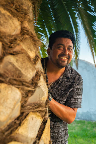 istock A man is quietly peeking out from behind a tall palm tree 2200741020