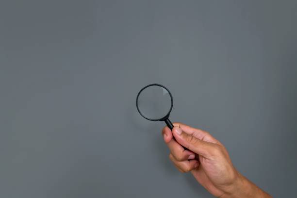 istock Man's hand holding a magnifying glass with copy space on a gray background 2200746764