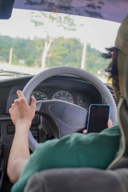 istock Image of driver engaging in dangerous texting while steering / risky smartphone use on the road 2200761370